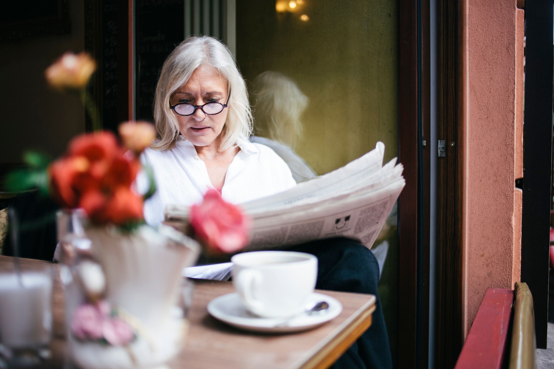 senior woman sits in a Sidewalk Cafe and reads newspaper